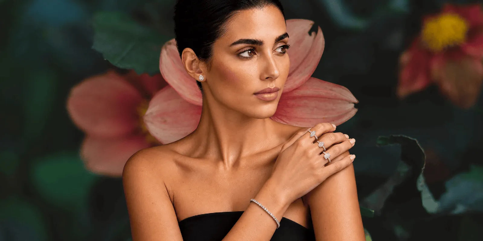 A woman wearing three SIA diamond engagement rings, a pear-shaped diamond earring and a diamond tennis bracelet